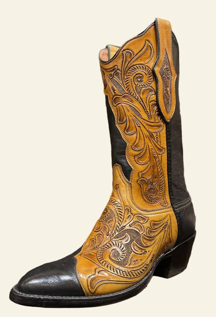 Cowboy boot with intricate leatherwork on a wooden block, with a background of more boots.