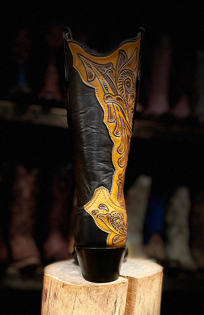 Black cowboy boot with gold embroidery on a wooden block against a dark background