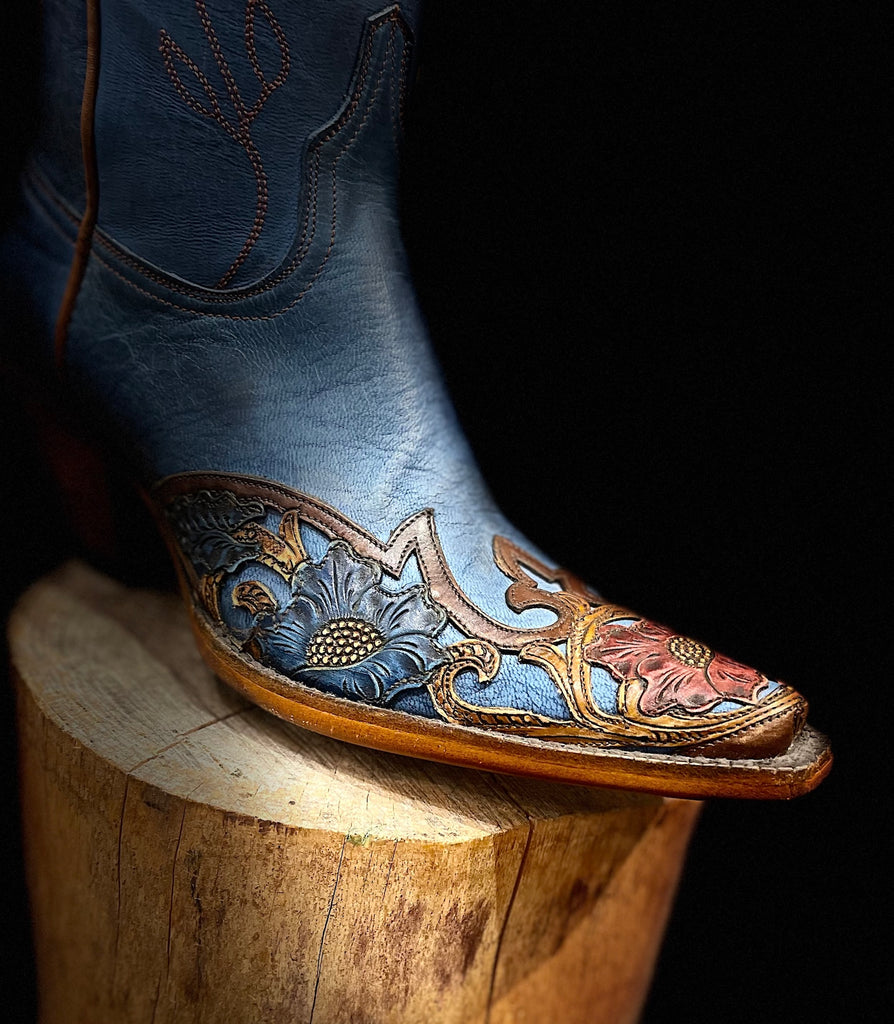 Blue cowboy boot with intricate leatherwork on a wooden block against a black background