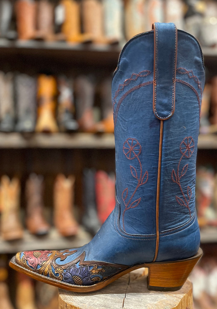 Blue embroidered cowboy boot on a wooden block with a blurred boot store background