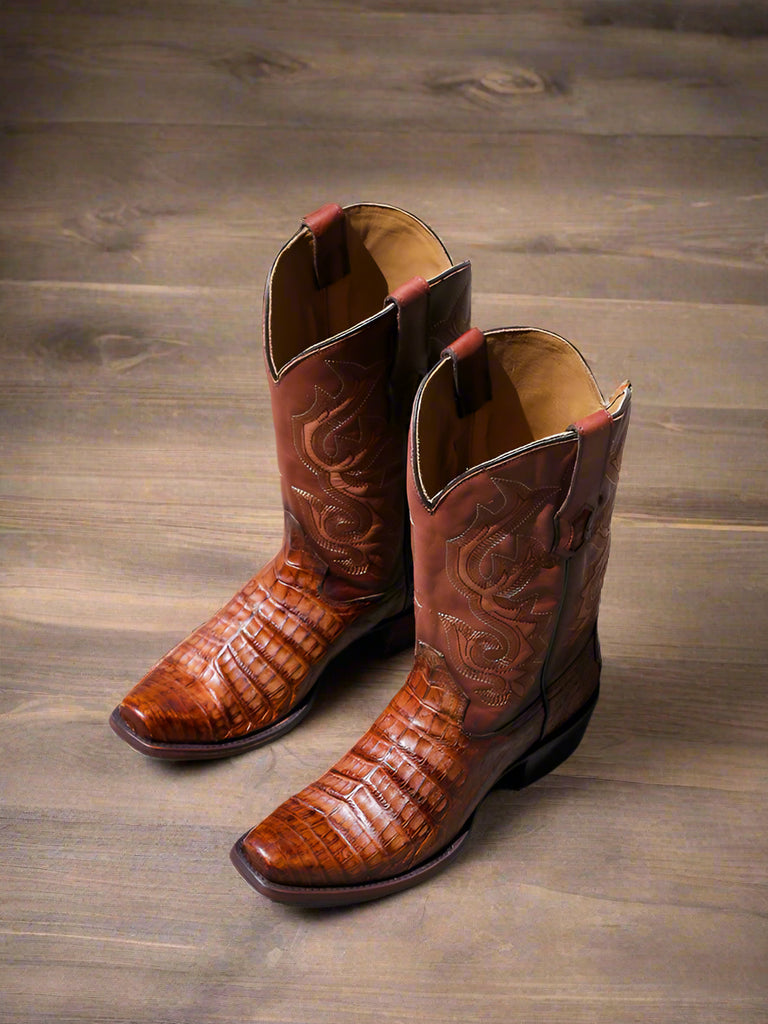 A pair of men's honey brown caiman narrow square toe cowboy boots on a wooden surface.