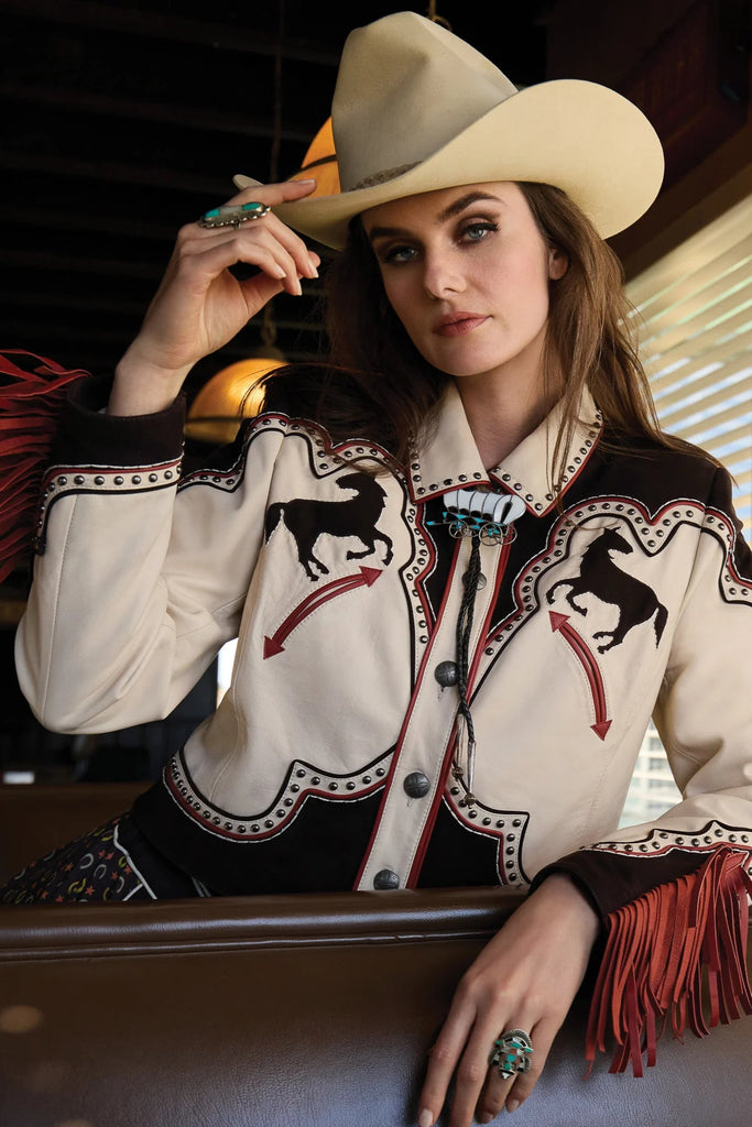 Woman wearing a western-style jacket with horse designs and a cowboy hat, sitting in a vehicle.