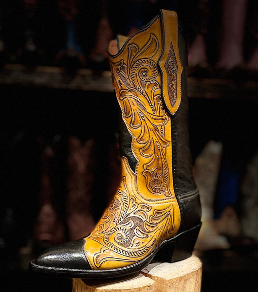 Cowboy boot with intricate yellow and black design on a wooden block against a blurred background