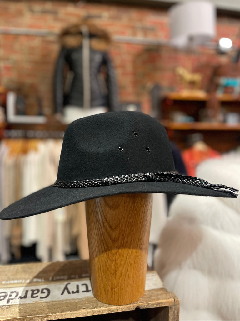 Black wide-brimmed hat with braided detail on a wooden block against a blurred store background