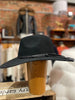 Black wide-brimmed hat with braided detail on a wooden block against a blurred store background