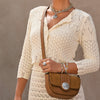 Woman holding a brown leather handbag wearing a beige knitted cardigan against a neutral background