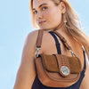 Woman wearing a brown leather crossbody bag against a clear blue sky