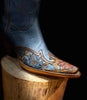 Blue cowboy boot with intricate leatherwork on a wooden block against a black background