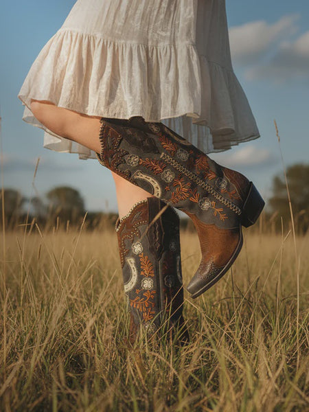 Women wearing floral and horseshoe embroidered cowboy boots in a field with a white dress.