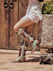 Woman wearing colorful hand tooled and painted Corral boots in front of a wooden door.
