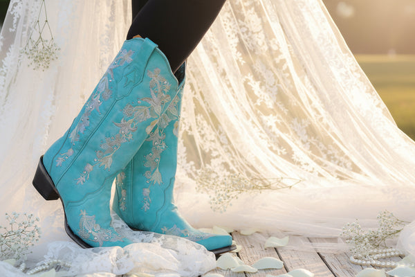 Turquoise cowboy boots with floral embroidery worn by a person in a garden setting.