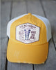 A distressed yellow and white cap hat with a front patch that reads 'DO NO HARM BUT TAKE NO BULL' and features a cow illustration, shown on a gray wooden surface.
