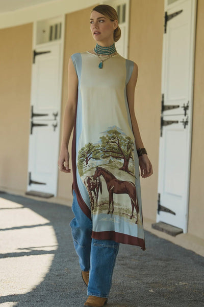 Woman wearing a long dress with horse design in front of barn doors.