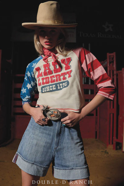 Women wearing a 'Lady Liberty Since 1776' shirt with an American flag design in a rustic setting.