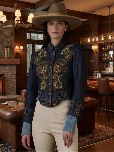 Woman wearing a dark blue embroidered jacket with gold details, beige pants, and a brown hat against a brown background.