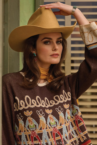Woman wearing a brown sweater with cowboy graphics and a tan cowboy hat.