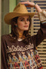 Woman wearing a brown sweater with cowboy graphics and a tan cowboy hat.