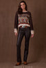 Woman wearing a patterned sweater and leather pants against a brown background