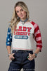 Woman wearing a colorful shirt with text and patterns, standing against a plain background.
