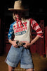 Person wearing a 'Lady Liberty Since 1776' shirt with American flag design in a rustic setting.