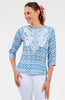 Woman wearing a blue patterned blouse with white pants on a white background