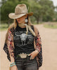 Woman wearing a cowboy hat, black t-shirt with graphic design, and floral kimono in an outdoor setting.