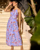 Woman in a blue floral dress standing on steps with greenery around