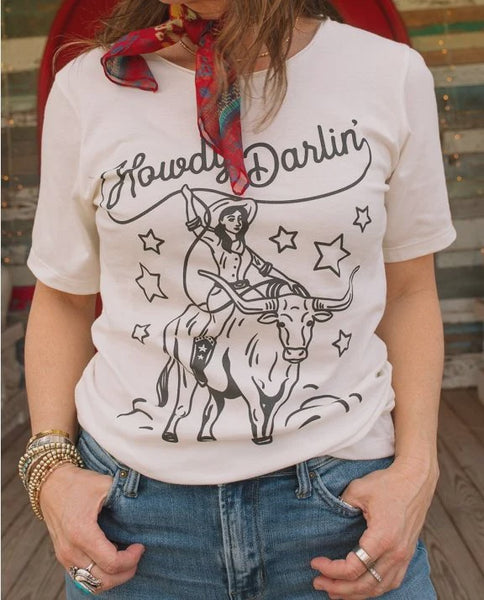 A woman wearing a white graphic t-shirt with a black cowboy and steer/bull illustration and the text 'Howdy Darlin''.