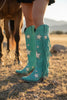 Turquoise cowboy boots with star patterns and fringes on a poolside background