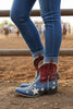 Red, white, and blue cowboy boots with star patterns worn by a person on a natural background.