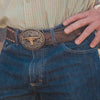 Close-up of a person wearing blue jeans with a decorative belt buckle featuring a bull design.