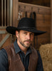 Black wide-brimmed hat with braided band on a wooden surface, blurred store interior background