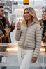 Woman in a beige Parajumpers puffer jacket holding a glass of champagne in a snowy outdoor setting.