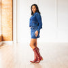 Woman wearing a denim outfit with red cowboy boots in a room with white walls and a brick wall.