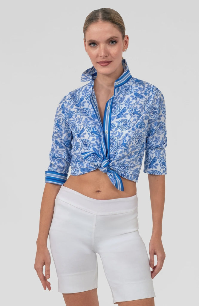 Woman wearing a blue patterned top and white shorts on a light gray background