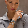 Woman wearing a smartwatch, earrings, and bracelets on a neutral background
