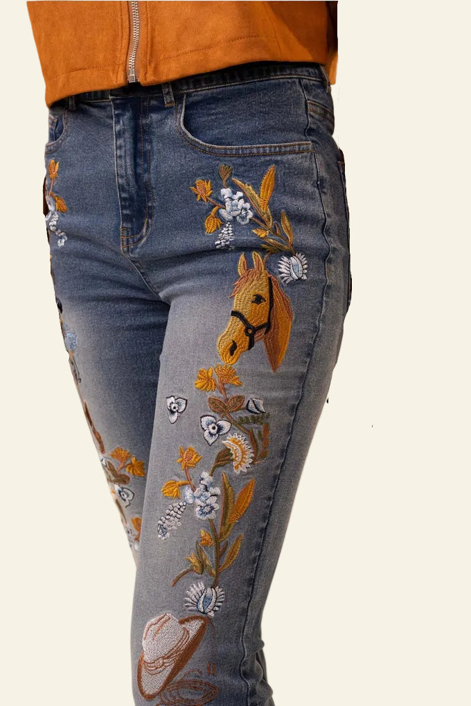 Embroidered jeans with horse design worn by a person against a beige background