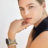 Woman wearing multiple bracelets and an earring on a plain background