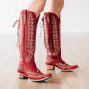 Red cowboy boots with intricate white patterns on a light wooden floor.